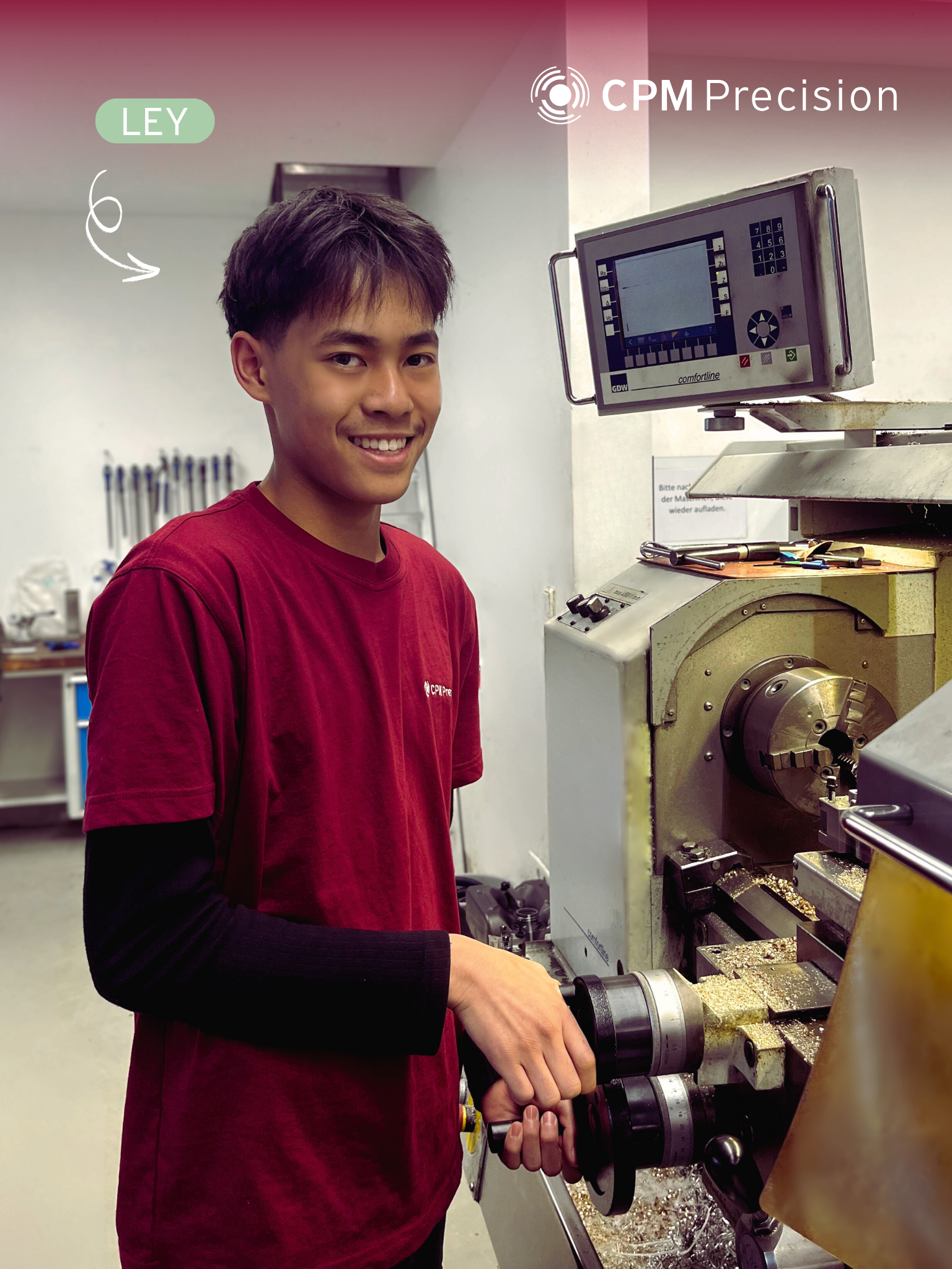 Ley, an apprentice at CPM Precision, is standing at a conventional lathe in the production hall and smiling at the camera.