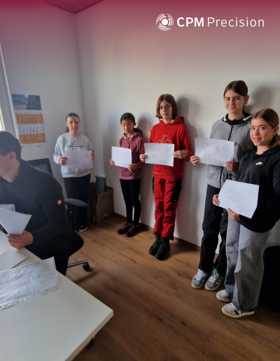 Girls stand in an office holding their own technical drawings while an employee explains the results at a computer.