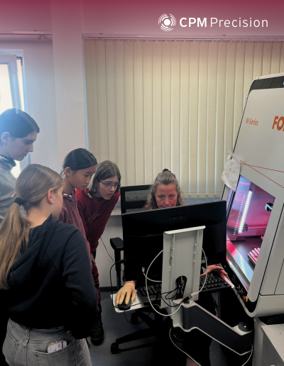Several girls observe the operation of an industrial laser marking system together with an employee.